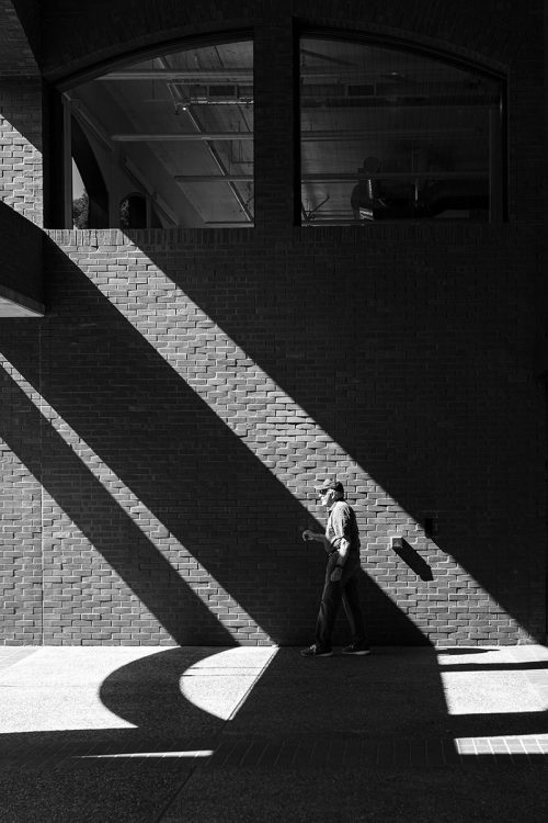 black and white Street photograph of man walking through the shadows
